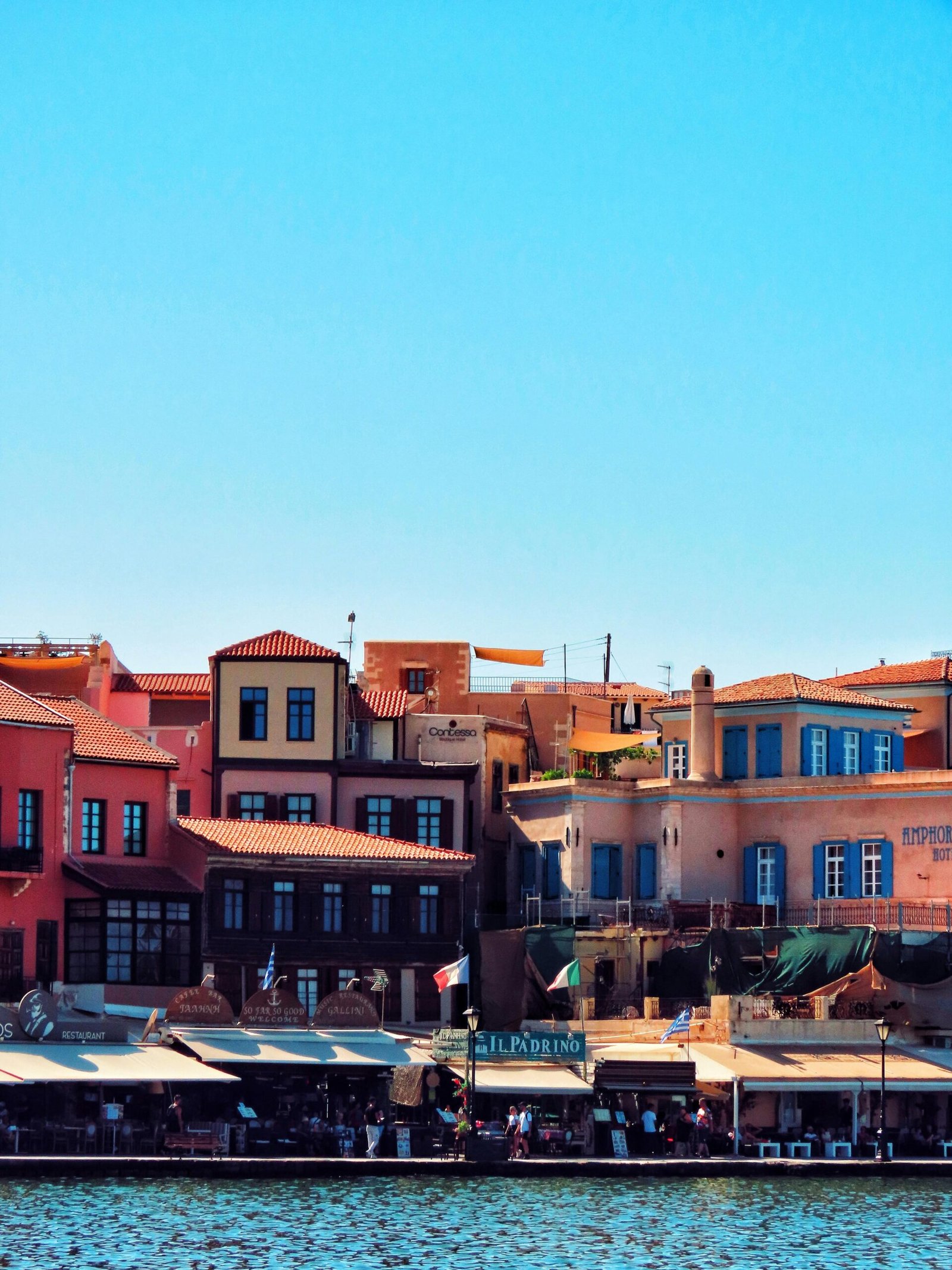 Charming view of the colorful Venetian harbor buildings in Chania, Greece against a clear blue sky.